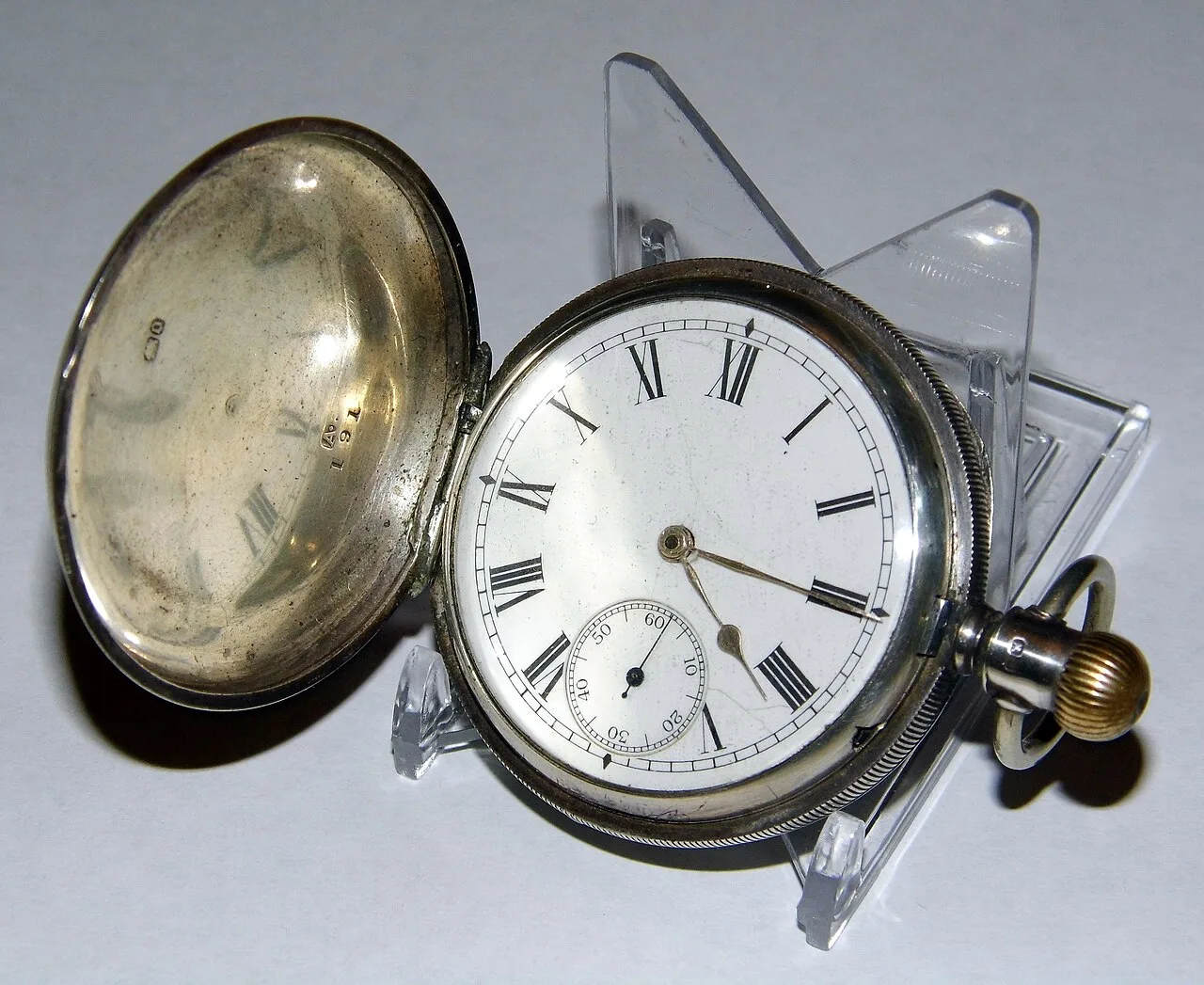 Silver hunting-case pocket watch open beside its white enamel dial, with small British hallmarks and a case number stamped inside the front cover