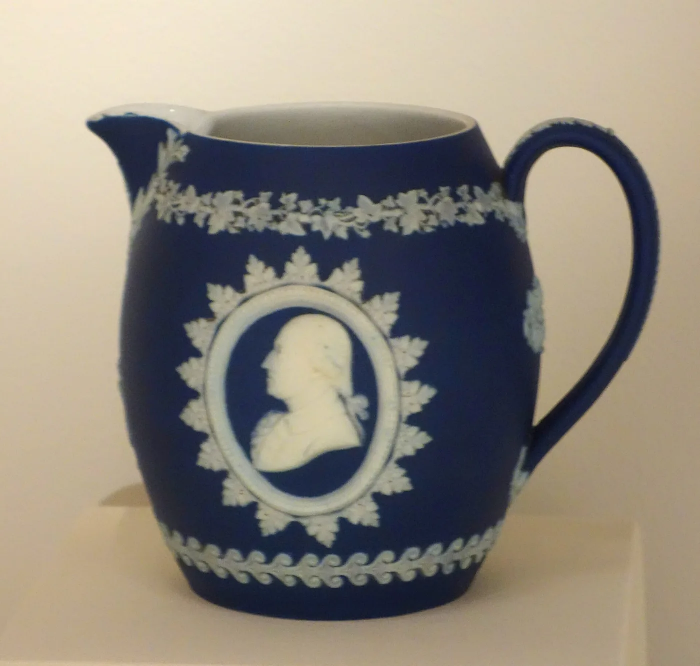 Dark blue Wedgwood jasper jug with a white portrait medallion in a star-shaped frame and a white interior at the rim